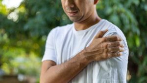 man gripping shoulder in pain outdoors
