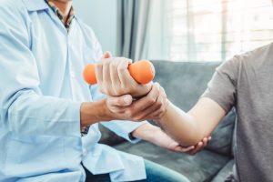 Physiotherapist helping male athlete perform Post-surgery rehab for Elbow pain suing an orange dumbell