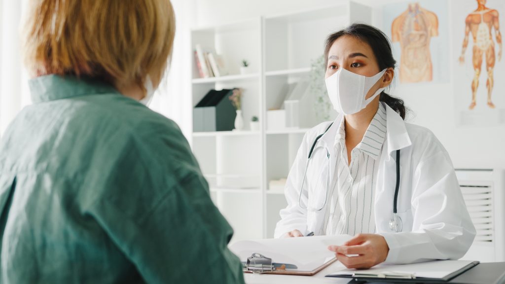 Lady physiotherapist wearing mask consulting a lady on sports physiotherapy options to aid recovery from injury